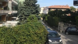 Een woonstraat met geparkeerde auto's, een grote altijdgroene boom en meerlaags gebouwen met balkons.