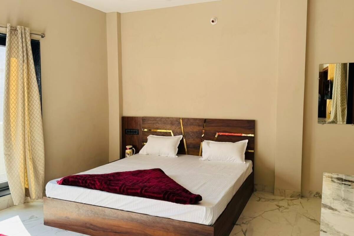 Een hotelkamer met een groot bed, een houten hoofdbord, een nachtkastje en een raam met gordijnen.