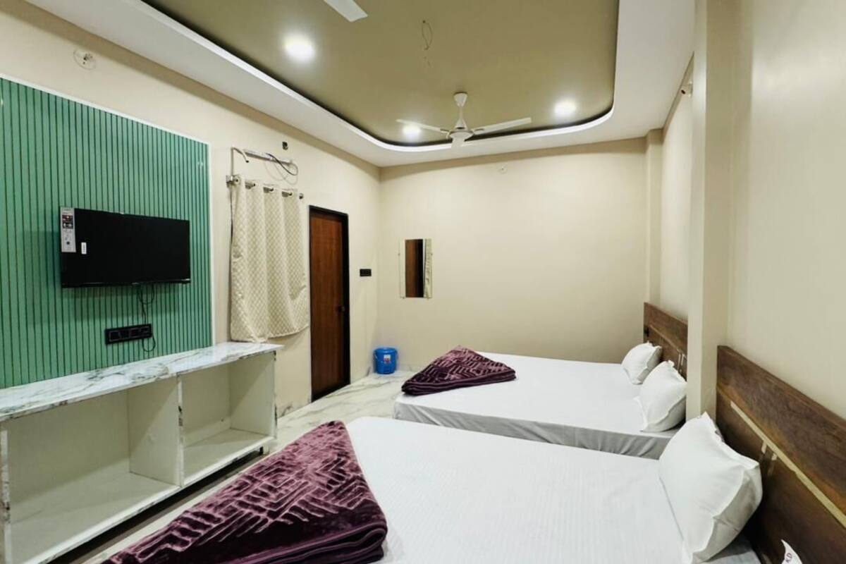 Hotelkamer met twee bedden, een televisie bevestigd aan een groen paneel, een plafondventilator en een klein raam.
