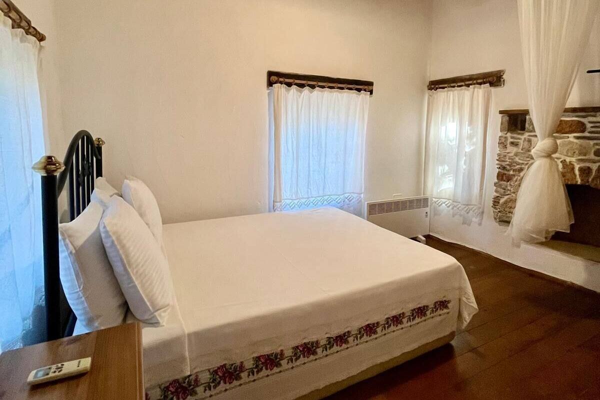 A bedroom with a large bed, wooden ceiling beams, and a stone wall.