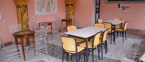 Comedor con suelo de mármol, sillas transparentes y mesas, con un ventanal grande y columnas decorativas.