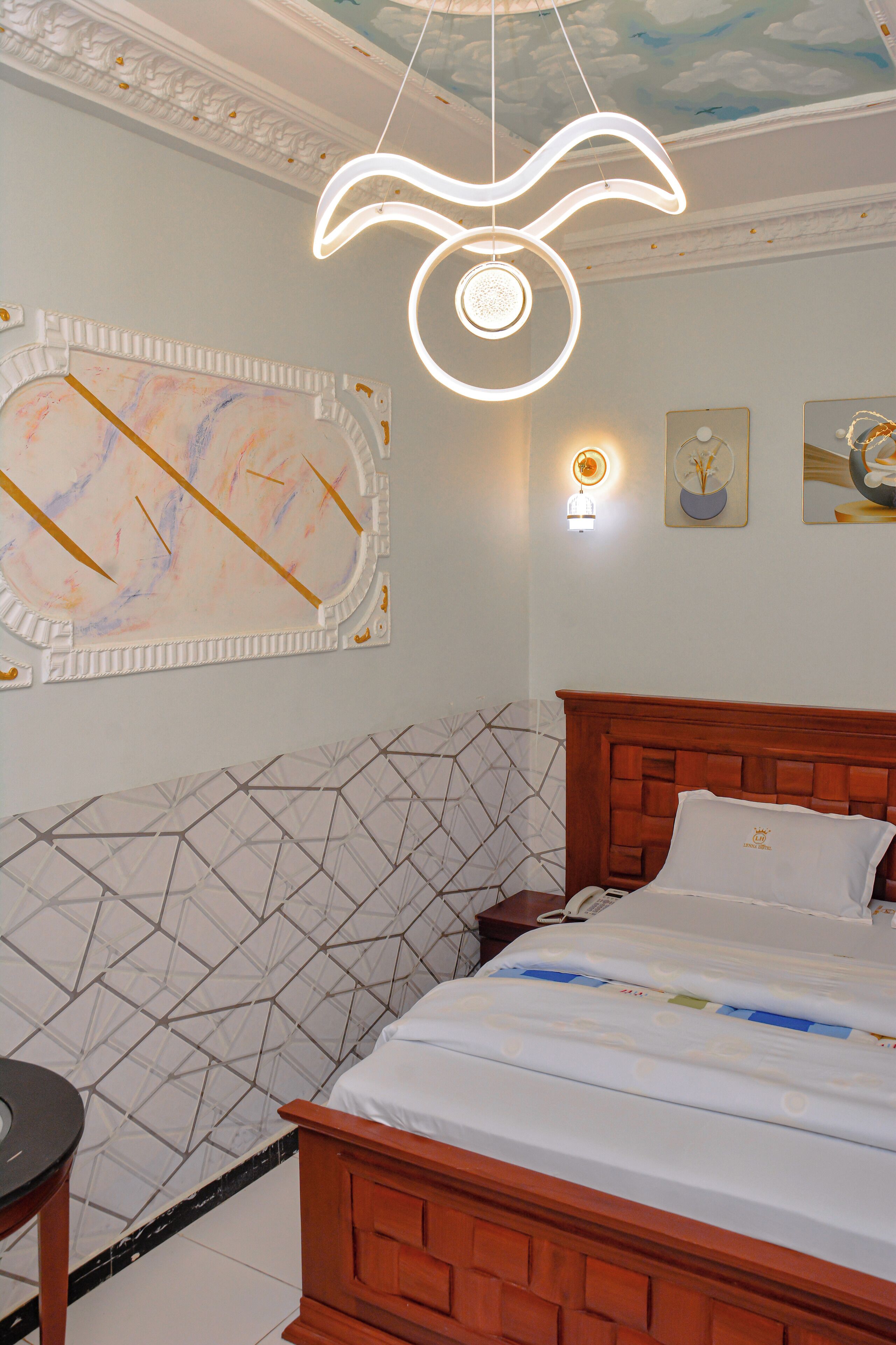 Un dormitorio con cabecera de madera, cama con ropa de cama blanca, pared con diseño geométrico y techo decorado con motivos de nubes.