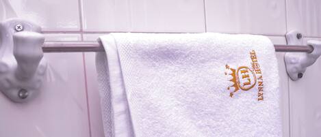 A white towel with a golden emblem hanging on a metal towel rack in a bathroom with patterned tiles.