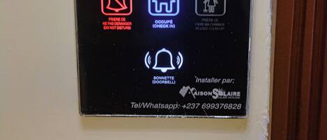 A hotel room number sign for Lynda Hotel, room A303, with icons for a do not disturb sign, a house icon, and a bell icon.