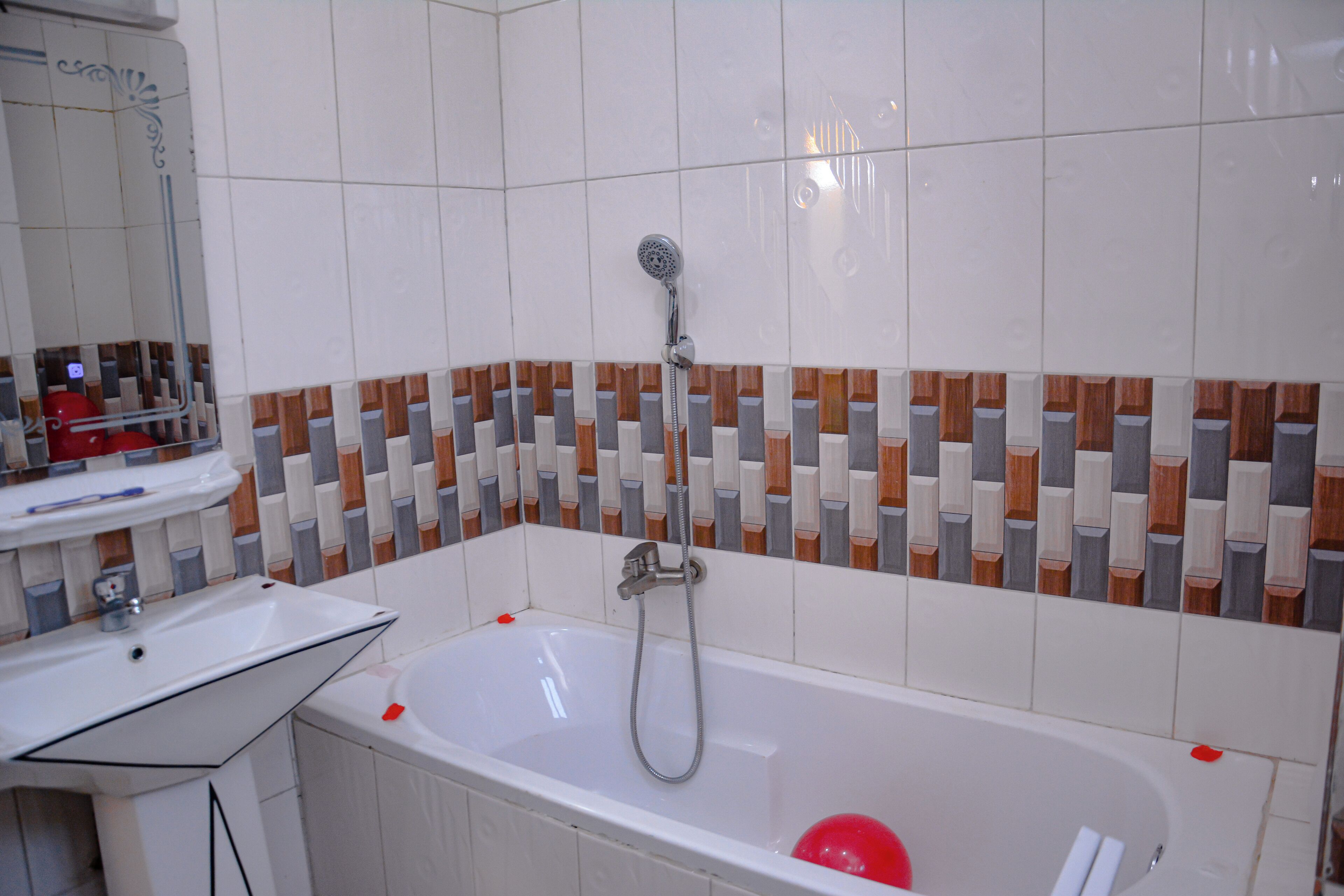 Un baño con una bañera blanca, un cabezal de ducha y un pared de azulejos con un diseño geométrico.