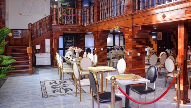 A spacious dining area with multiple tables and chairs, a wooden staircase, and a chandelier. - lynna hôtel (Yaoundé)
