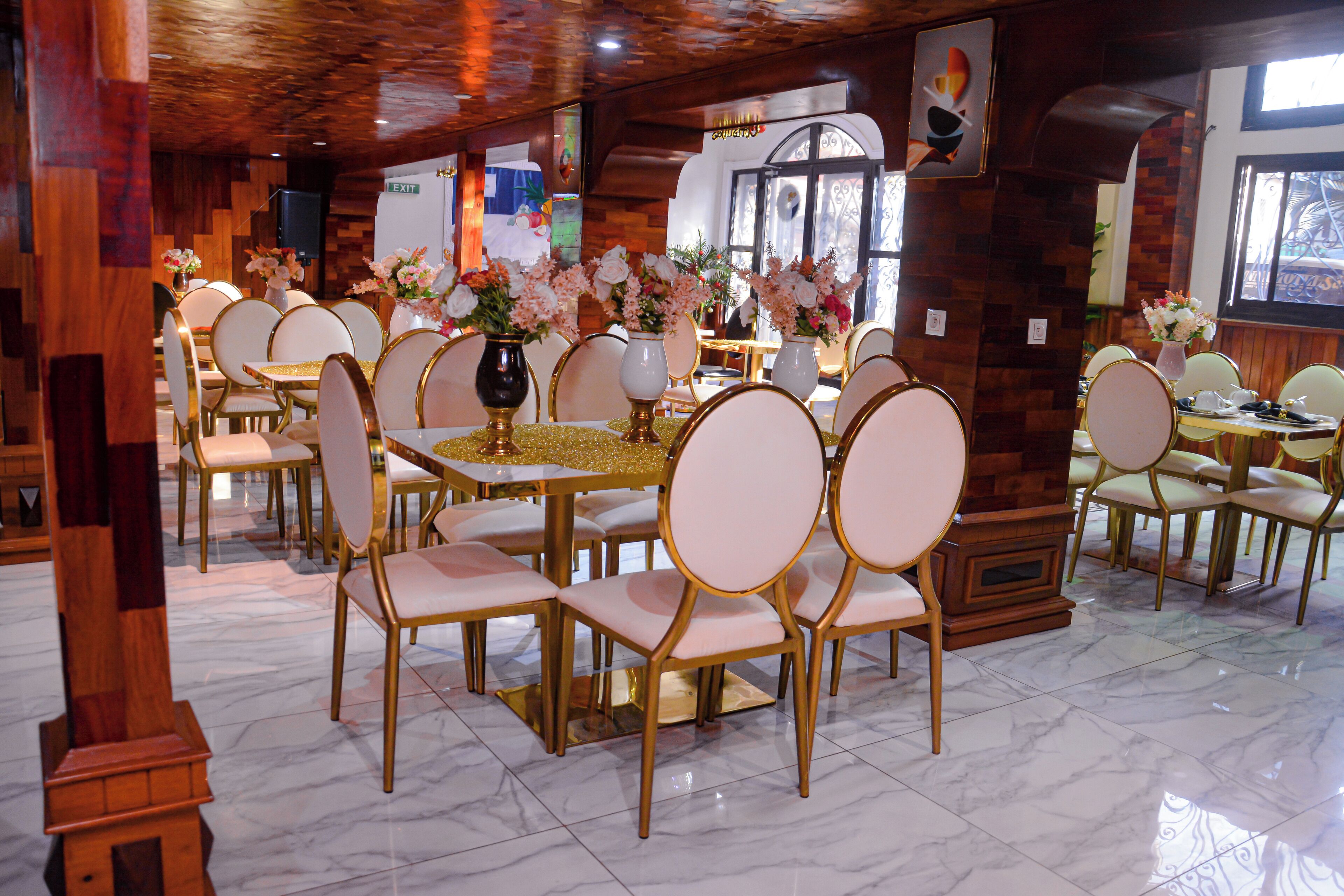 A restaurant with marble flooring, gold and white chairs, and floral centerpieces on tables.