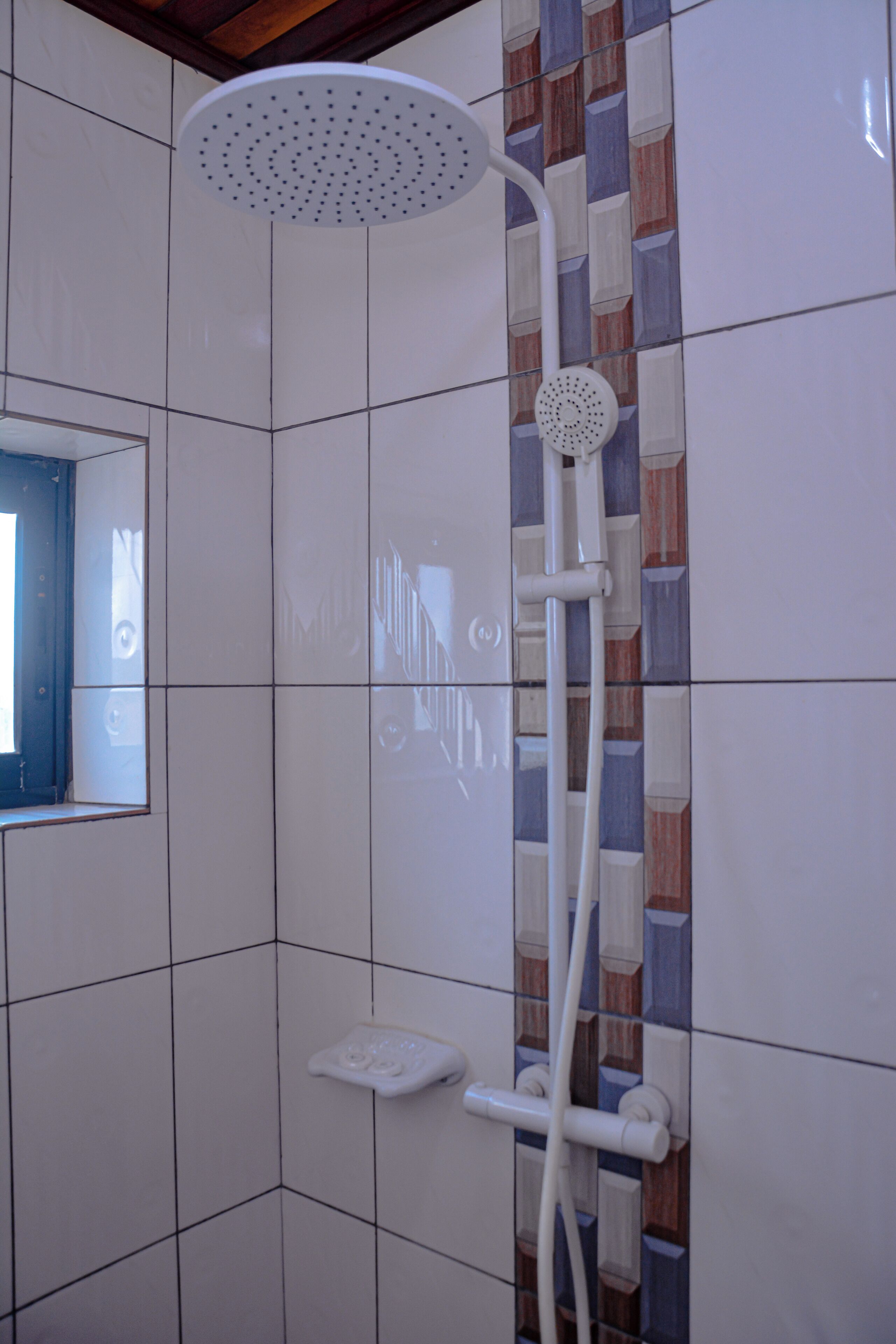 A shower with a handheld showerhead and a wall-mounted control panel.