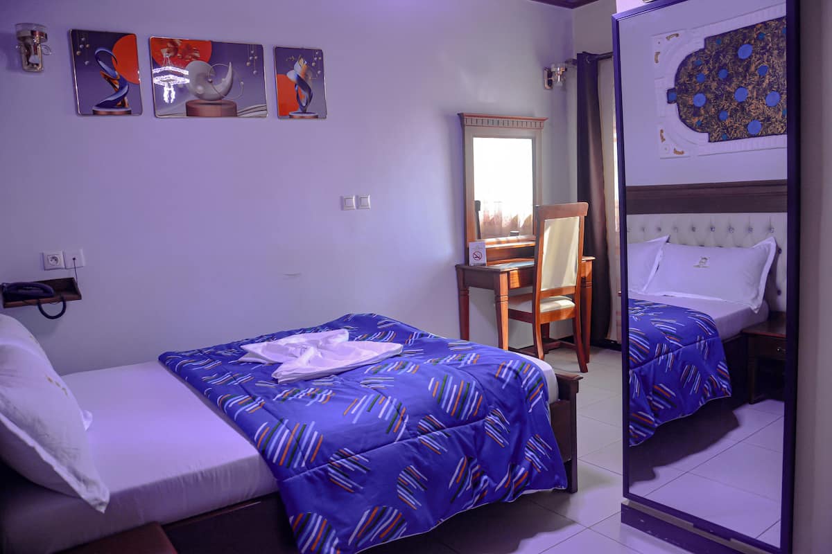 A hotel room with two beds, a mirror, a chair, and artwork on the walls.