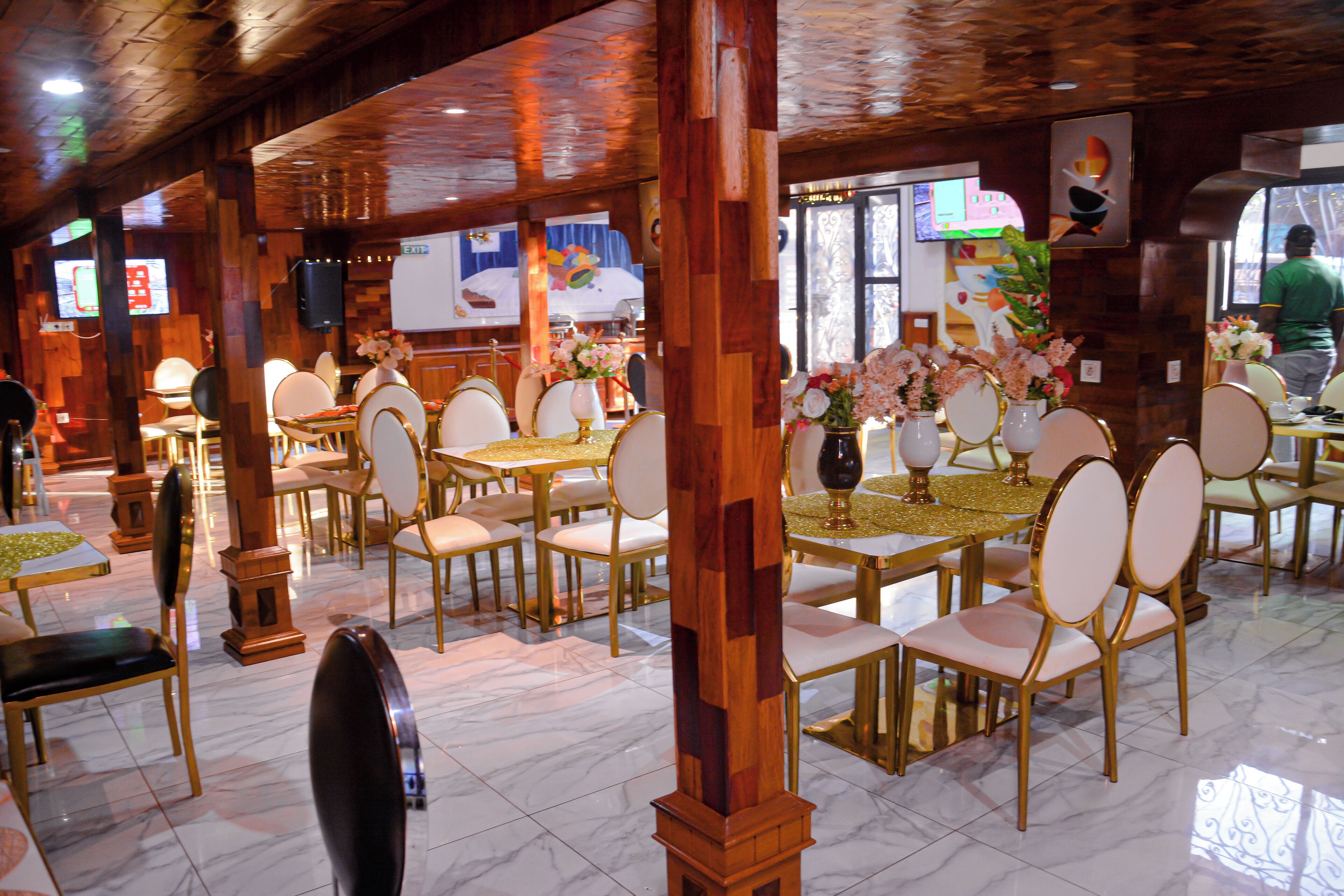 A restaurant with wooden pillars, marble flooring, and tables with gold accents.