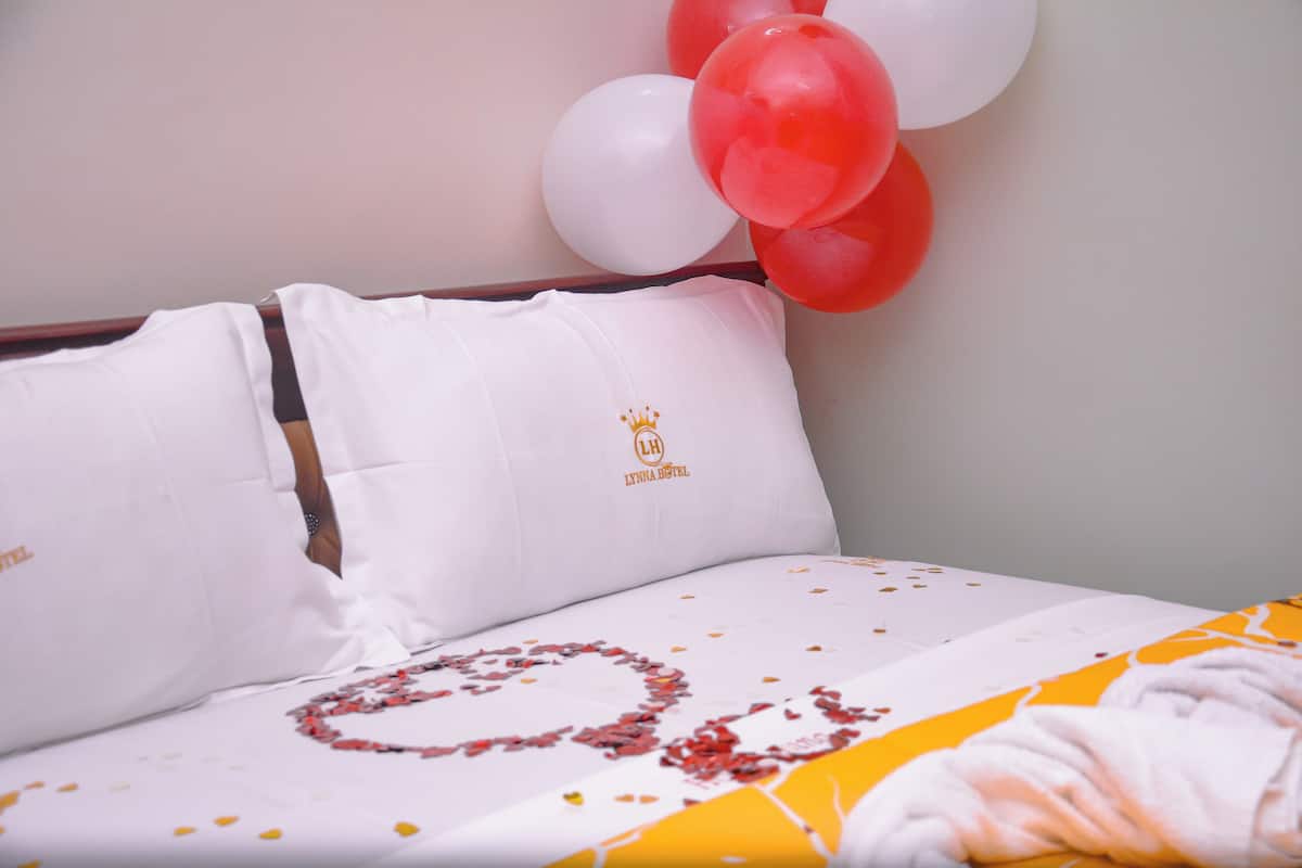 A hotel room with a neatly made bed, a pillow with a logo, and a wall decorated with balloons.