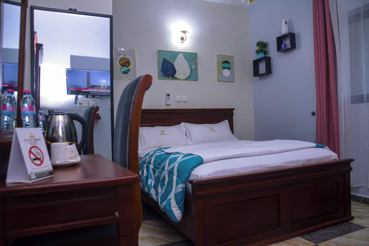 A neatly made bed with a wooden headboard, a desk with a chair, a wall-mounted TV, and a door with a pink curtain.