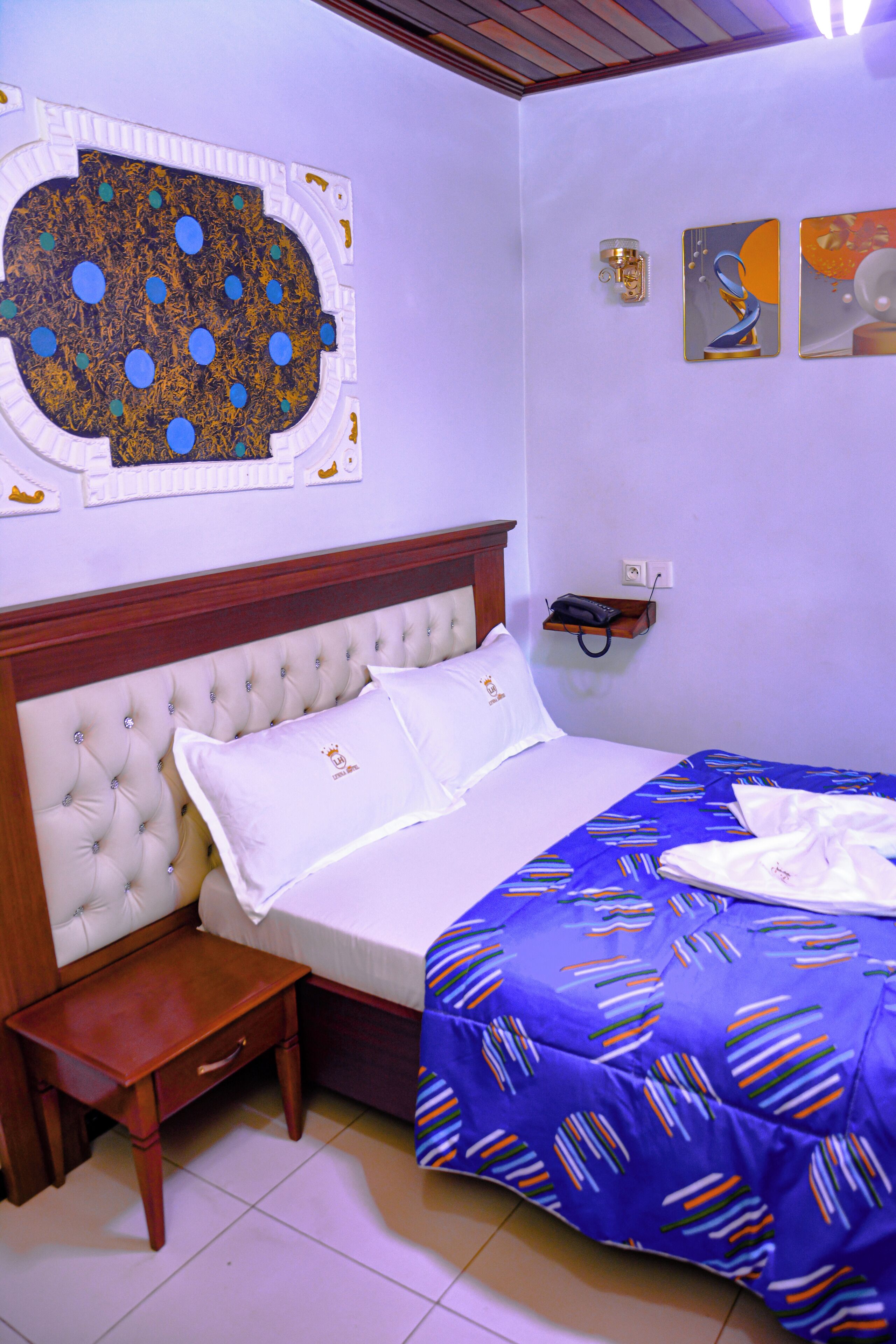 A neatly made bed with a blue patterned bedspread, a wooden headboard, and a small bedside table.