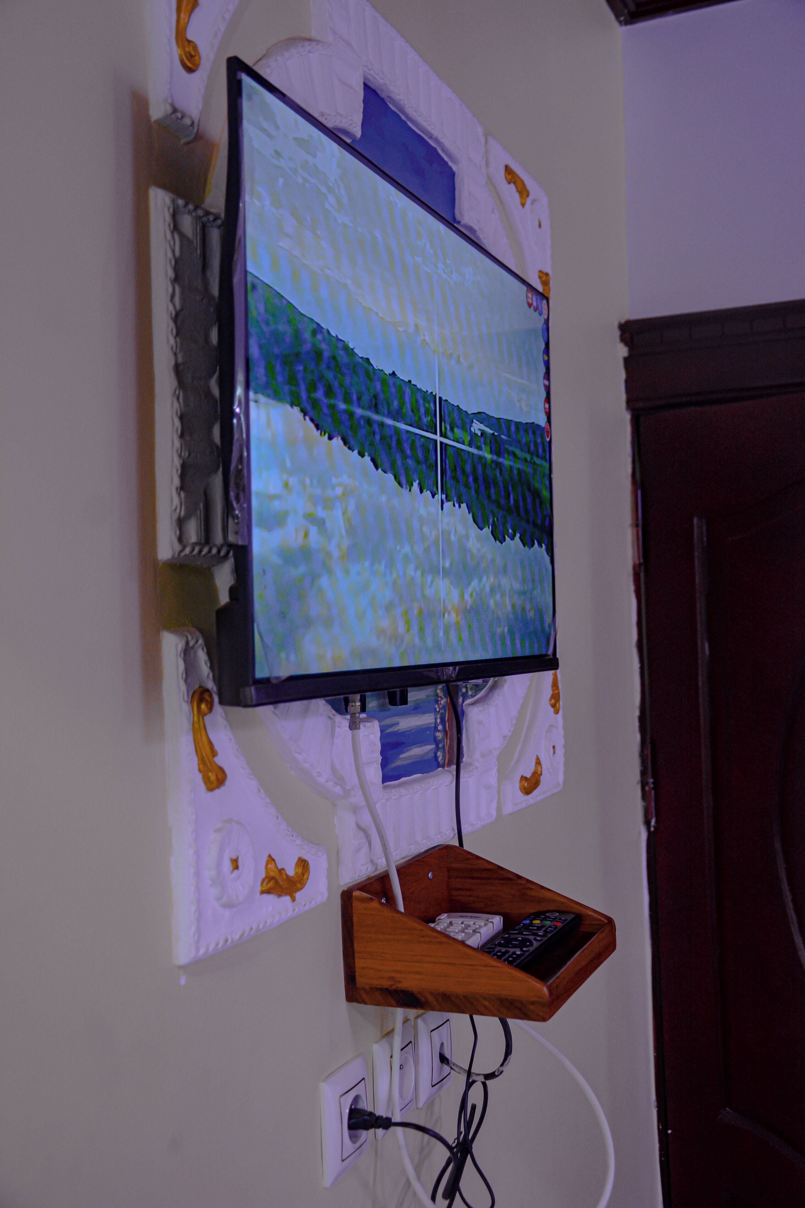 A television mounted on a wall with a wooden shelf below it.