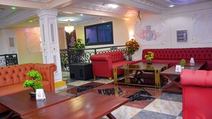 A lobby with red sofas, a wooden coffee table, and a potted plant. - lynna hôtel (Yaoundé)