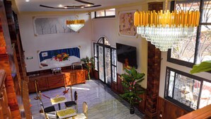 A hotel room with a bed, a TV, a dining area with chairs and a table, and a chandelier. - lynna hôtel (Yaoundé)