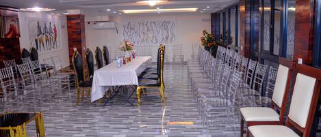 Une salle de banquet avec une longue table, des chaises transparentes et un sol à motifs.