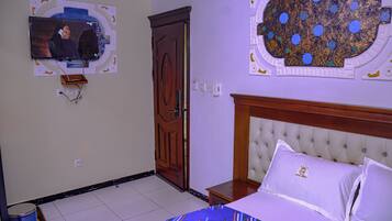 Habitación de hotel con cama, televisión montada en la pared, puerta de madera y techo decorativo.
