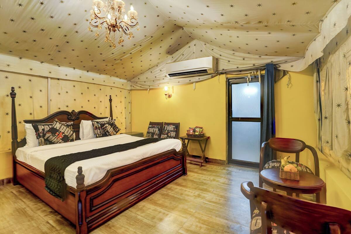Un dormitorio con cama de madera, un candelabro, un equipo de aire acondicionado, una mesita con una cesta y una silla.