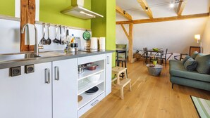 Una cucina con mobili bianchi, soffitto in legno e zona pranzo con divano verde.