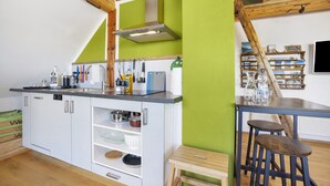 Cucina con mobili bianchi, soffitto in legno e una parete verde decorativa.