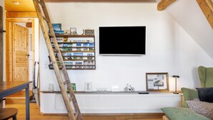 Una stanza con una scala in legno, un termosifone bianco, una televisione a muro e uno scaffale con diversi oggetti.