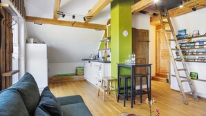 Un accogliente soggiorno con divano, travi in legno, una cucina con frigorifero bianco e una parete verde a contrasto.