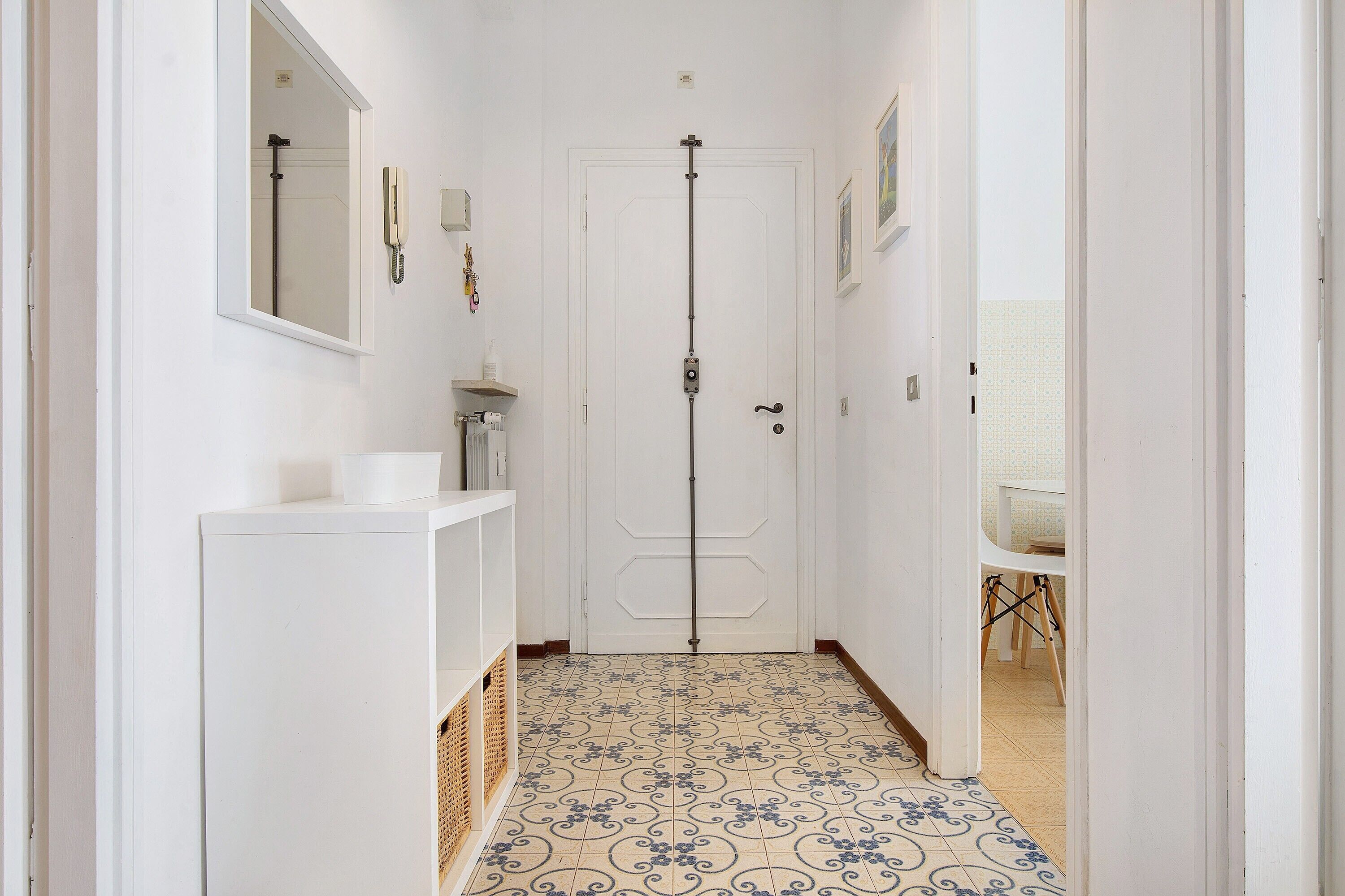 A narrow hallway with a white door, a small sink, and a patterned floor.