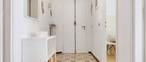 A narrow hallway with a white door, a small sink, and a patterned floor.