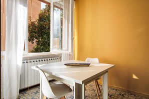 Una habitación con una mesa blanca, una silla, un ventanal con cortinas y un radiador.