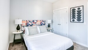 A bedroom with a bed, two bedside tables, a nightstand, a colorful abstract painting, and a door. - TWO CozySuites Music Row Lovely Condo in Nashville (Nashville)