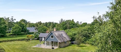A house with a thatched roof, surrounded by a well-maintained lawn and dense greenery.