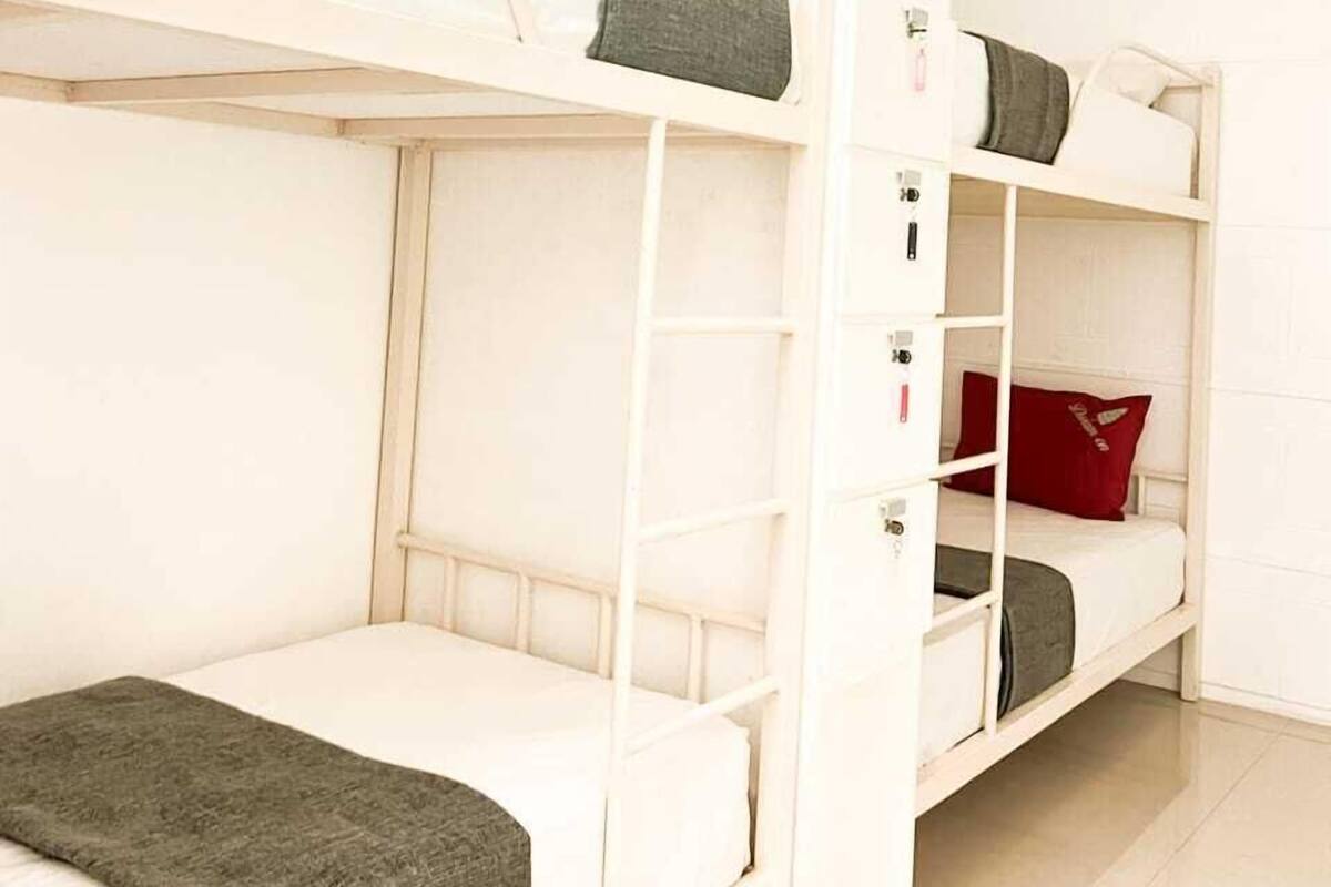 Une chambre avec des lits superposés, un puits de lumière, des murs blancs et un aménagement épuré et minimaliste.