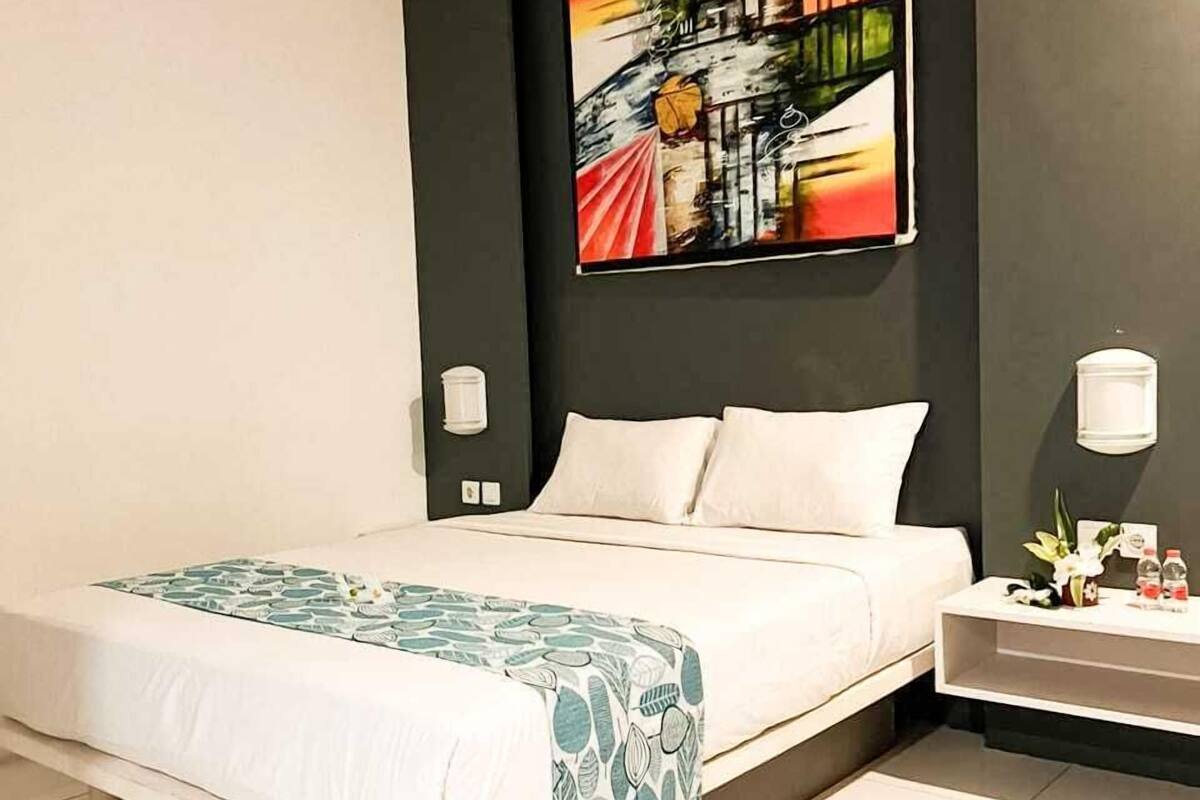 Une chambre d’hôtel moderne avec un grand lit, une table de chevet, une lampe fixée au mur et une peinture abstraite aux couleurs vives au-dessus du lit.
