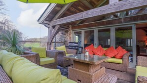 An outdoor patio with wicker furniture, a glass table, and a bright green umbrella. - Kerslake House (Torpoint)