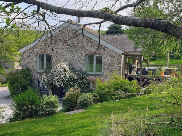 A stone house with a porch, surrounded by greenery and a gravel driveway.