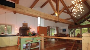 A spacious kitchen with wooden beams, a large island with stools, and a view of the outdoors. - Kerslake House (Torpoint)