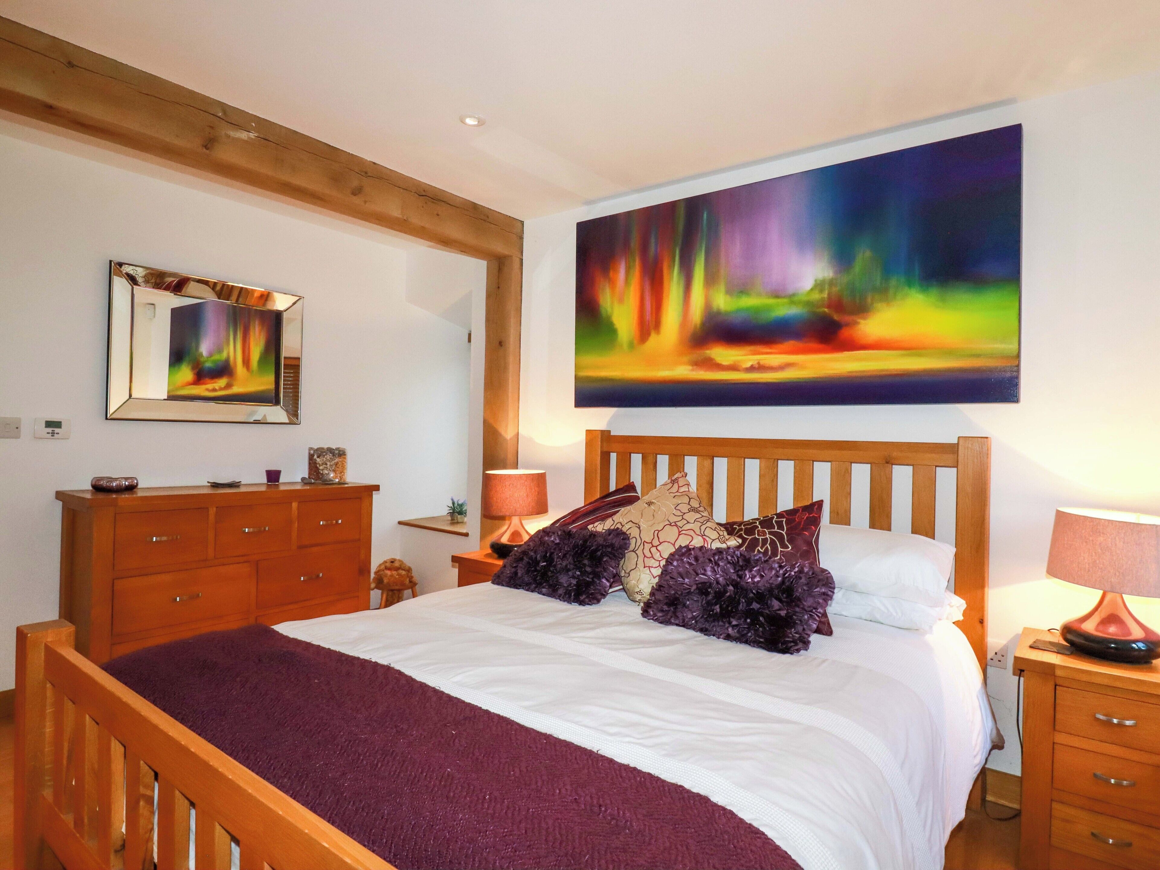 A bedroom with a wooden bed, a nightstand, a dresser, and a large painting of a colorful aurora borealis.