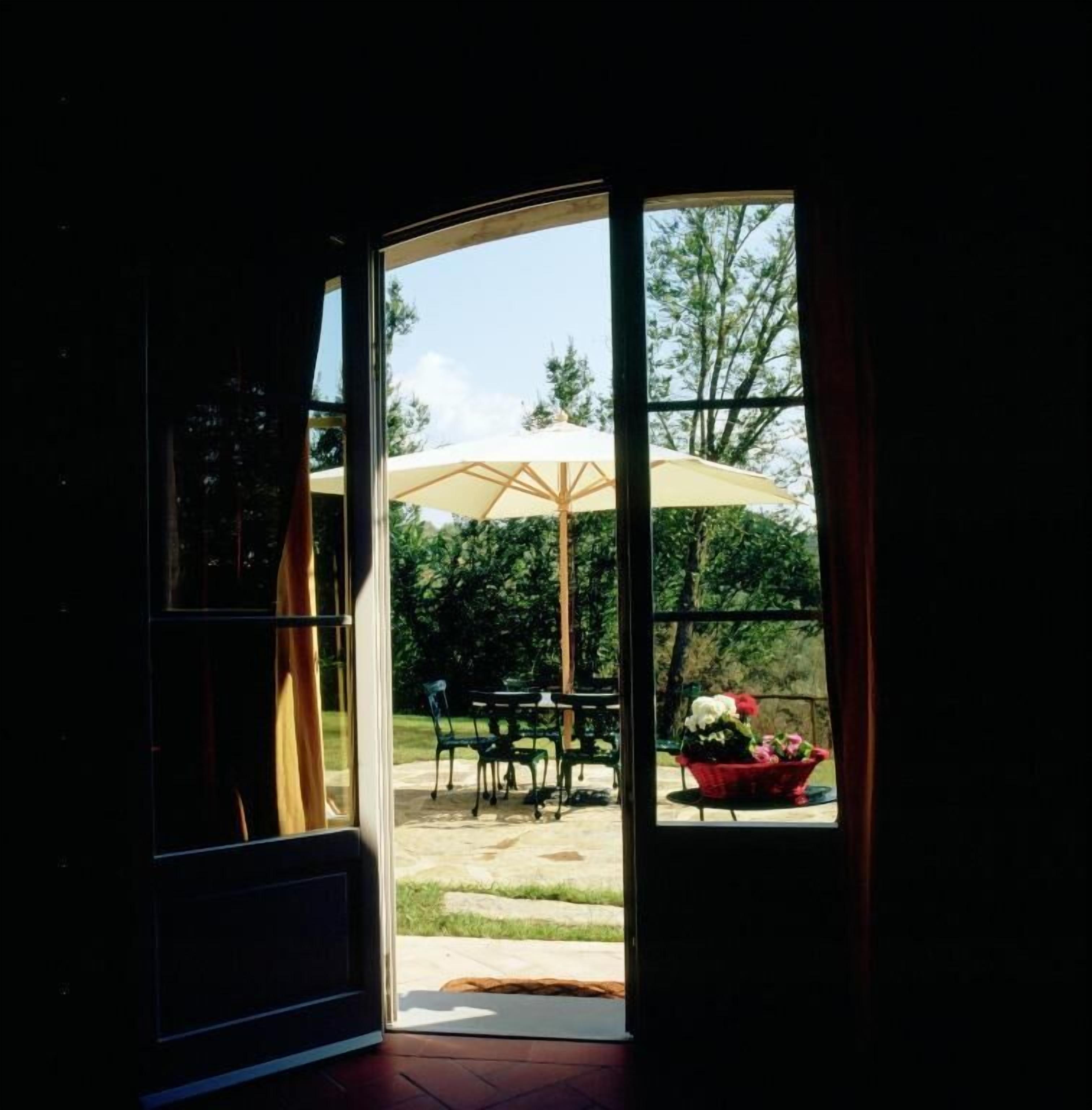 An open door leading to an outdoor patio with a table, chairs, and a large umbrella.
