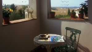 Une pièce avec une table et des chaises, une fenêtre donnant sur la campagne et une cage à oiseaux suspendue.
