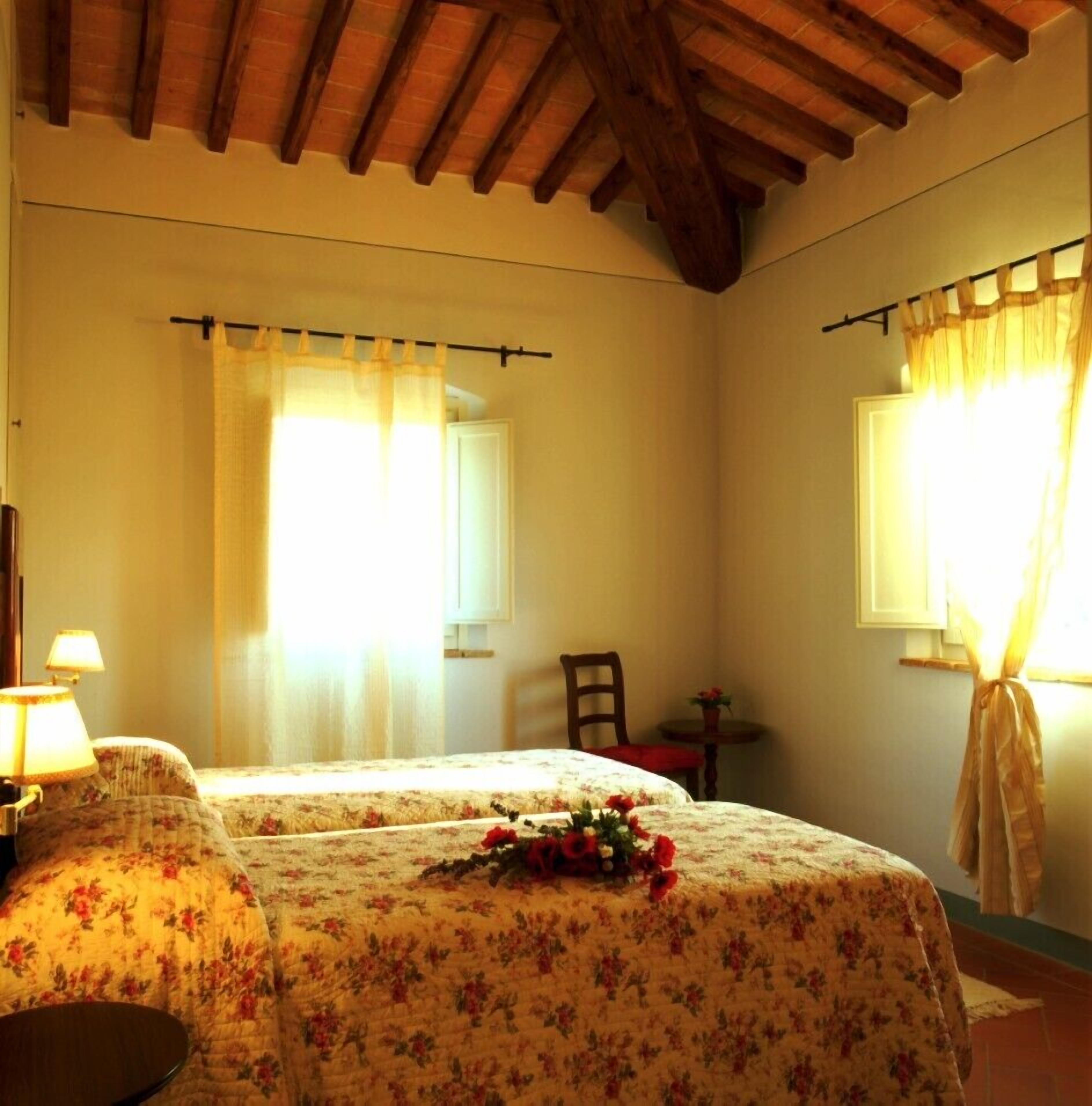 Een slaapkamer met twee bedden, een stoel, een tafel en een raam met gordijnen.