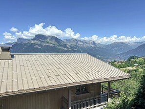 A wooden building with a sloped roof, a balcony, and a view of mountains in the background. - 3-Room Apartment with Parking and Mont Blanc Views (Combloux)