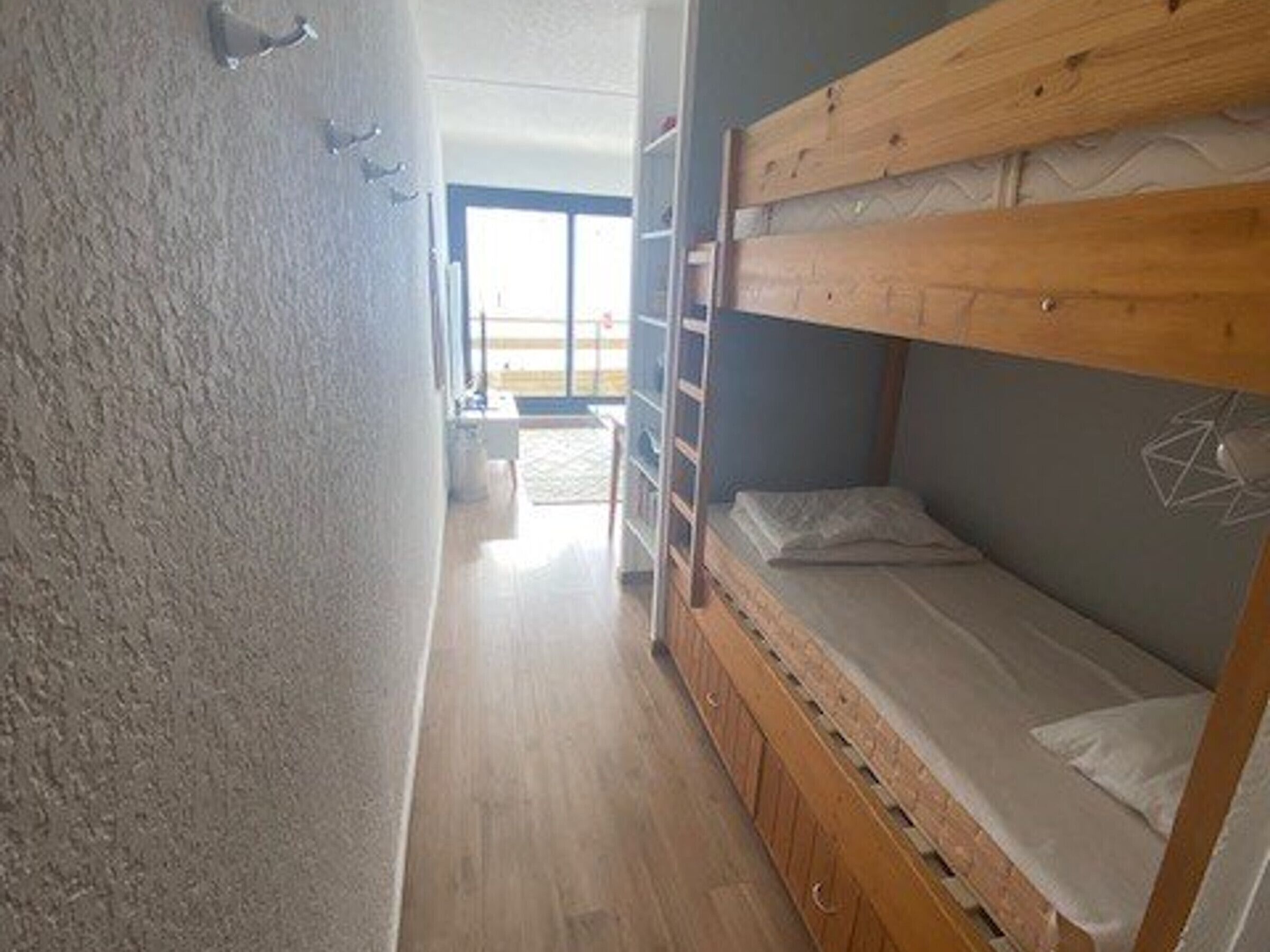 Une chambre avec un lit superposé en bois, une échelle et un mur blanc.