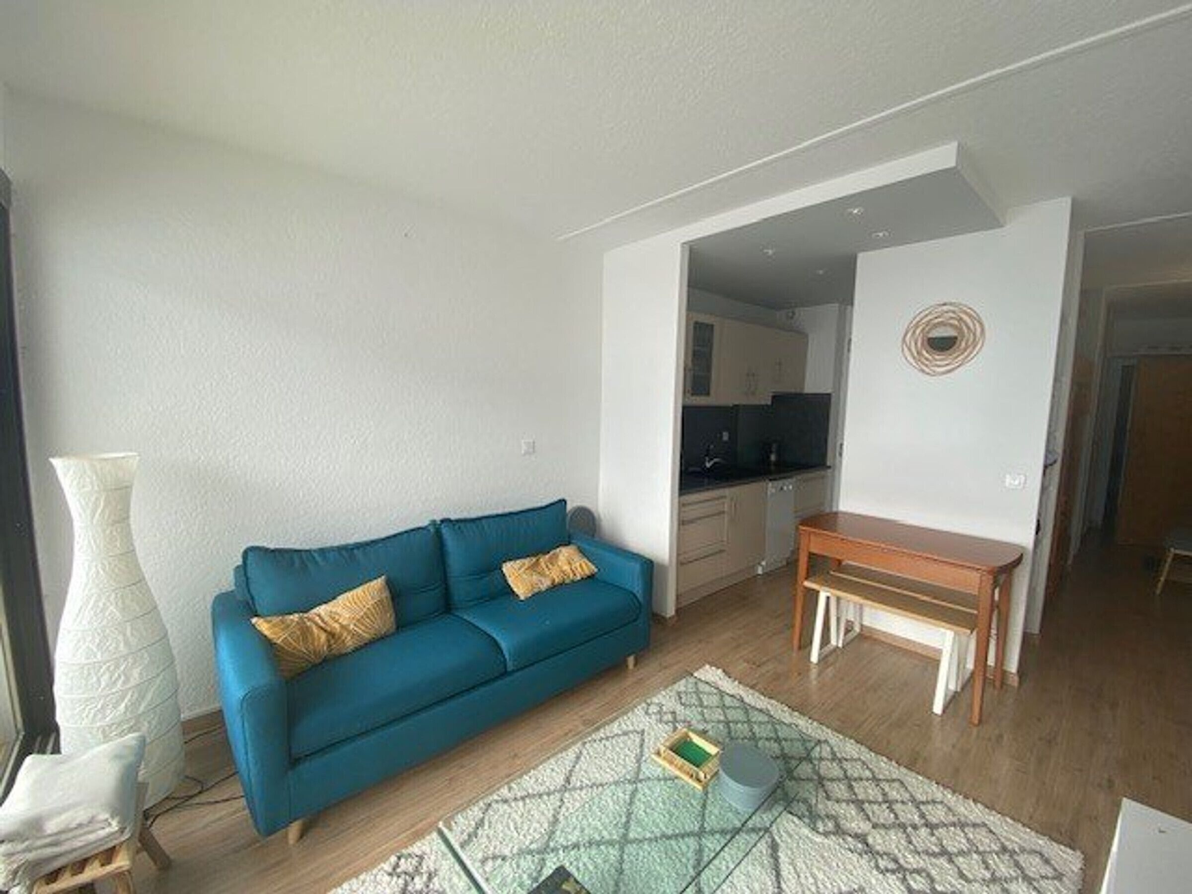 Un salon avec un canapé bleu, une petite table en bois et un tapis à motifs.