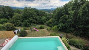 Une piscine dotée d’une terrasse en bois, entourée d’une végétation luxuriante et offrant une vue sur les montagnes lointaines.