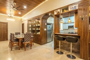 A modern kitchen with wooden cabinetry, a built-in stove, and a bar area with two stools. - Elivaas Leo's Den 4BHK With Private Pool (Greater Noida)