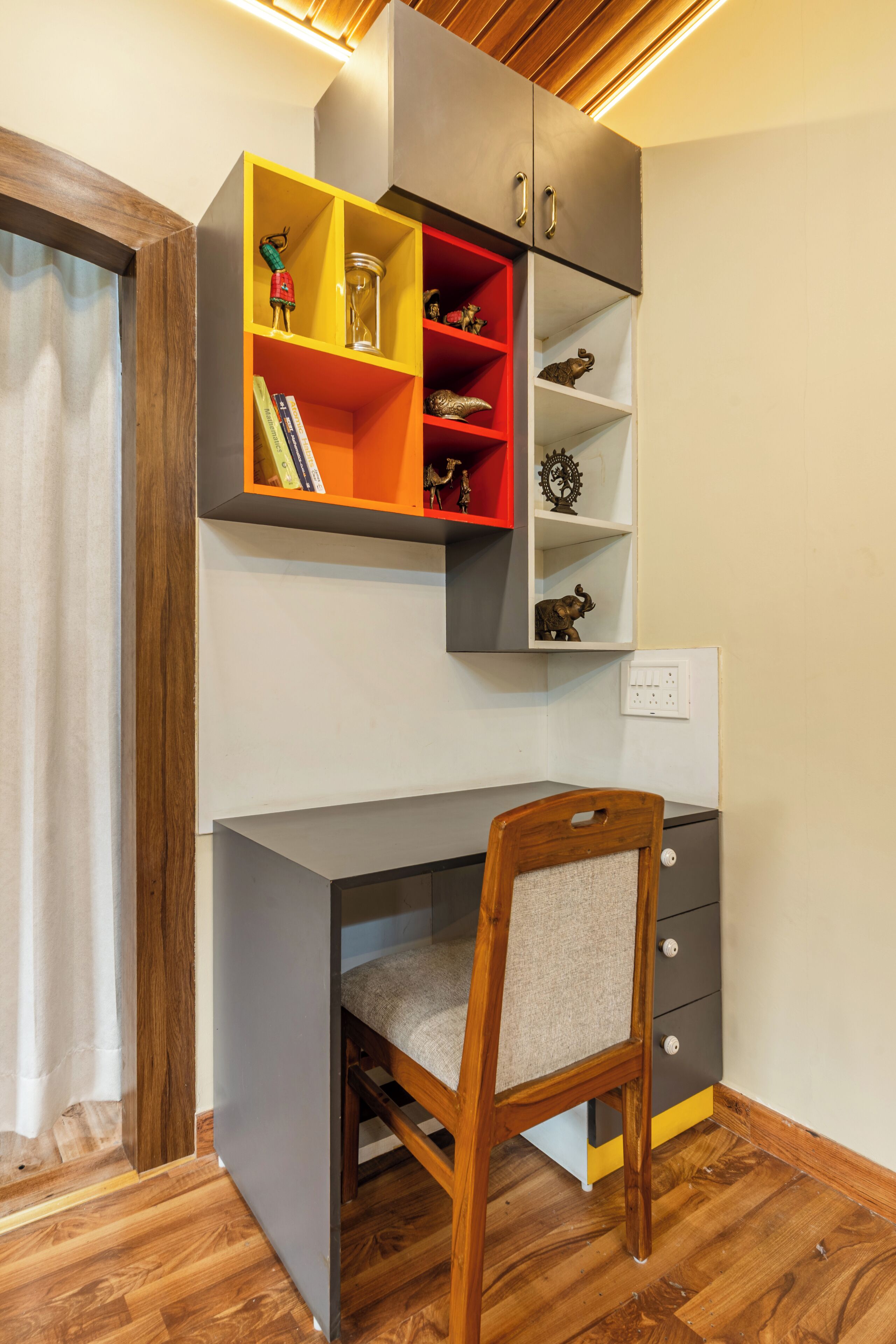 Un espacio de trabajo con escritorio, silla y estanterías empotradas llenas de libros y objetos decorativos.