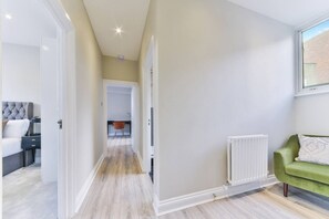 Eine moderne Wohnung mit Flur, der zu einem Schlafzimmer führt, einem Wohnbereich mit einem grünen Sofa und einem sichtbaren Heizkörper.