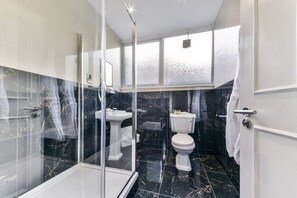 Un bagno con cabina doccia in vetro, un lavandino, un water e un'ampia finestra.