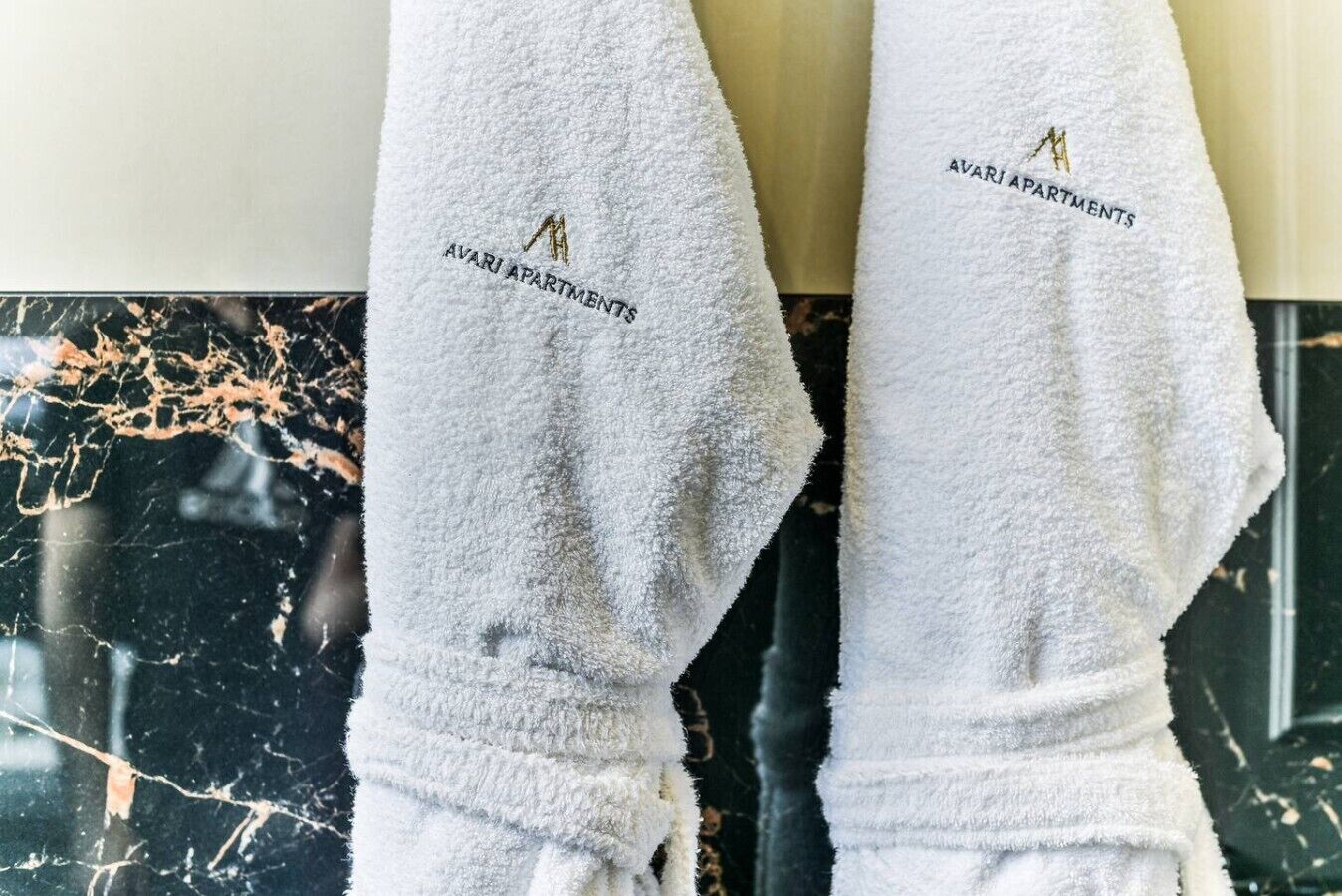 A pair of white towels with embroidered text and a logo, hanging on a marble surface.